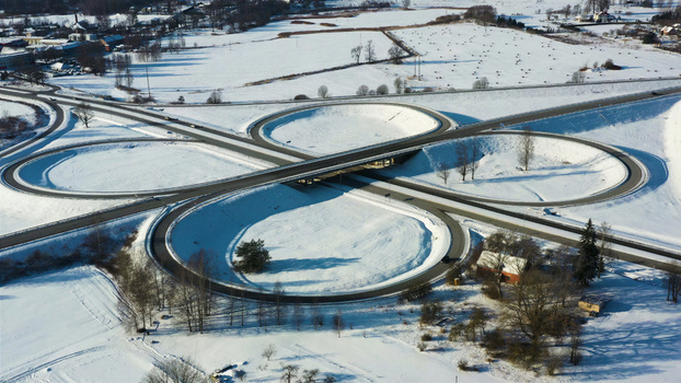 Aerial view of a snow covered cloverleaf highway interchange surrounded by winter fields and trees in Latvia. Aerial view of a snow covered cloverleaf highway interchange surrounded by winter fields and trees in Latvia.
