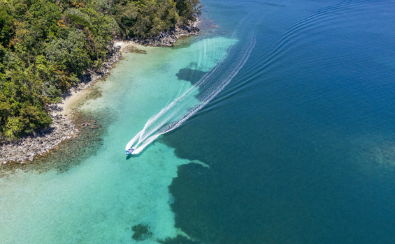 Aerial view of a motorboat leaving a white wake in turquoise tropical waters along the lush green coastline of Guanaja Bay Islands Department Honduras. Aerial view of a motorboat leaving a white wake in turquoise tropical waters along the lush green coastline of Guanaja Bay Islands Department Honduras.