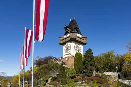 View of the clock tower standing tall on a hill with flags waving in the wind against a blue sky Graz Styria Austria. View of the clock tower standing tall on a hill with flags waving in the wind against a blue sky Graz Styria Austria.