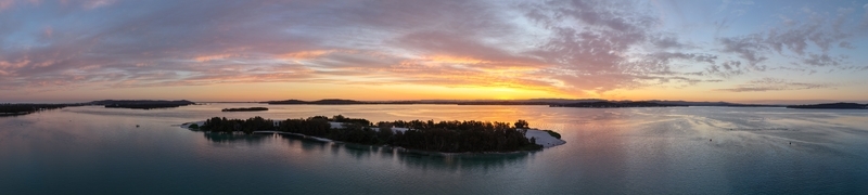 Aerial view of a tranquil lake reflecting the vibrant sunset hues with islands and lush trees dotting the landscape Newcastle New South Wales Australia.