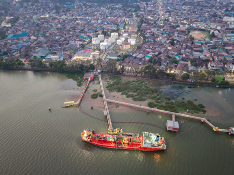 Aerial view of PT. Pertamina TBBM Samarinda oil terminal with a red tanker ship docked at the pier surrounded by dense residential rooftops in Samarinda Kalimantan Timur Indonesia.