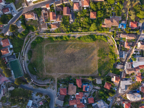 Aerial view of a grassy sports field surrounded by residential houses with red tiled roofs and lush green trees in Kruje Durres County Albania.