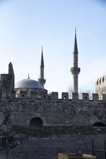 View of the historic stone walls of Kayseri Castle with the minarets and dome of a mosque rising behind them under a clear blue sky in Kayseri Kayseri Turkiye. View of the historic stone walls of Kayseri Castle with the minarets and dome of a mosque rising behind them under a clear blue sky in Kayseri Kayseri Turkiye.