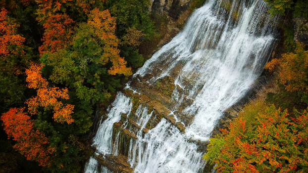 Aerial view of cascading Herisson Waterfalls amidst the vibrant autumn foliage a tapestry of orange and green hues Le Frasnois Bourgogne Franche Comt&eacute; France.