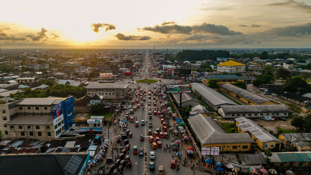 Aerial view of a busy roundabout with heavy traffic street vendors and urban buildings under a golden sunset sky in Uyo Akwa Ibom Nigeria. Aerial view of a busy roundabout with heavy traffic street vendors and urban buildings under a golden sunset sky in Uyo Akwa Ibom Nigeria.