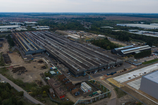 Aerial view of a large industrial factory complex with long multi gabled roofs surrounded by green space and infrastructure in the United Kingdom. Aerial view of a large industrial factory complex with long multi gabled roofs surrounded by green space and infrastructure in the United Kingdom.