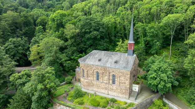 Aerial view of St. Menas church with its tall spire and stone walls nestled within a lush green forest on a hillside in Koblenz Rheinland Pfalz Germany. Aerial view of St. Menas church with its tall spire and stone walls nestled within a lush green forest on a hillside in Koblenz Rheinland Pfalz Germany.