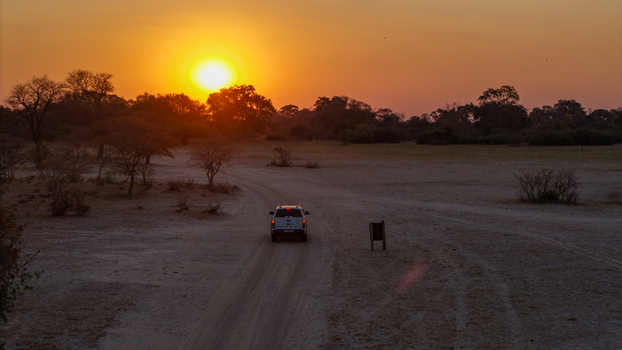 Aerial view of a vehicle driving along a dirt road through the savanna landscape during a vibrant sunset in the Okavango Delta North West District Botswana. Aerial view of a vehicle driving along a dirt road through the savanna landscape during a vibrant sunset in the Okavango Delta North West District Botswana.