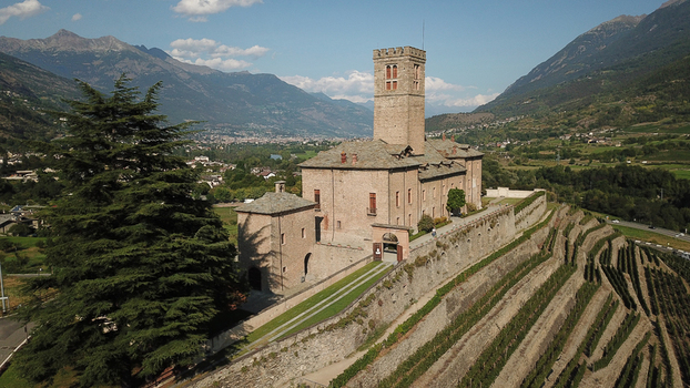 Aerial view of the historic Sarre Royal Castle featuring its prominent stone tower and terraced vineyards nestled in the mountains of Aosta Valley Italy. Aerial view of the historic Sarre Royal Castle featuring its prominent stone tower and terraced vineyards nestled in the mountains of Aosta Valley Italy.