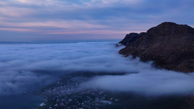 Aerial view of thick clouds rolling over mountain slopes and coastal residential areas during twilight in Cape Town Western Cape South Africa. Aerial view of thick clouds rolling over mountain slopes and coastal residential areas during twilight in Cape Town Western Cape South Africa.