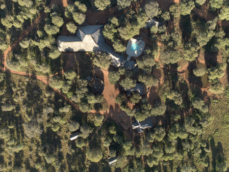 Aerial view of the thatched roofs and swimming pool at Tumbeta Private Game Reserve surrounded by dense bushveld and dirt paths in Thabazimbi Limpopo South Africa.