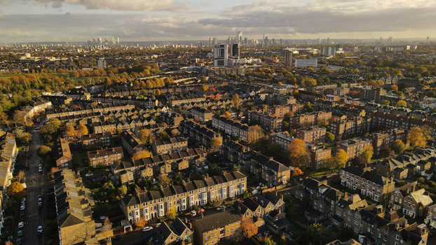 Aerial view of residential streets with rows of terraced houses autumn trees and the distant London skyline under a cloudy sky in London England United Kingdom.