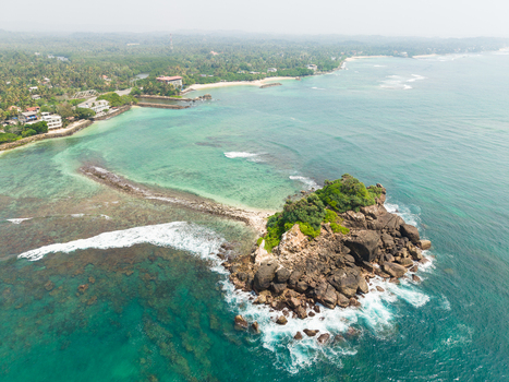 Aerial view of Devil s Rock island surrounded by turquoise ocean waters and lush tropical coastline Ahangama Southern Province Sri Lanka. Aerial view of Devil s Rock island surrounded by turquoise ocean waters and lush tropical coastline Ahangama Southern Province Sri Lanka.