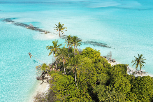 Aerial view of a lush tropical island with tall palm trees and dense vegetation surrounded by crystal clear turquoise lagoon water Innafinolhu Haa Alif Atoll Maldives. Aerial view of a lush tropical island with tall palm trees and dense vegetation surrounded by crystal clear turquoise lagoon water Innafinolhu Haa Alif Atoll Maldives.