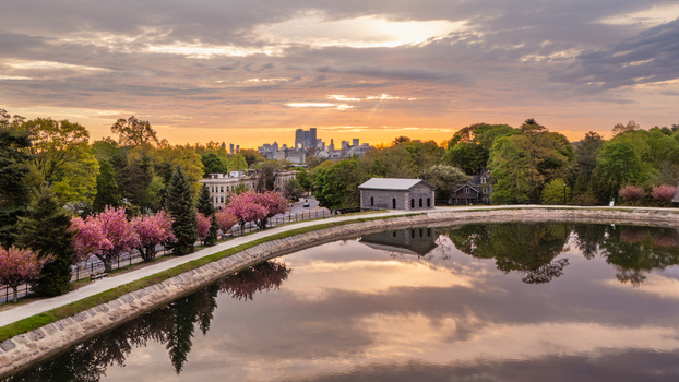 Aerial view of Brookline Reservoir with its stone gatehouse and blooming cherry blossoms against the distant Boston skyline at sunrise. Brookline Massachusetts United States.