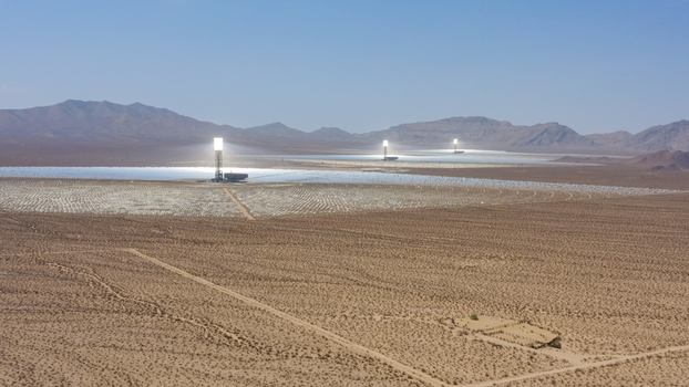 Aerial view of a large concentrated solar power plant with thousands of mirrors and central solar towers in a desert landscape in the United States.