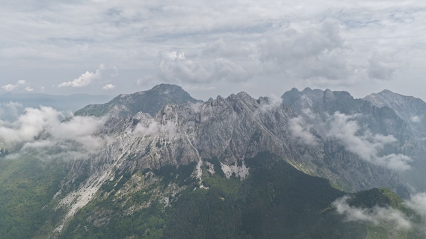 Aerial view of the rugged Apuan Alps with marble quarries and lush green slopes partially covered by clouds near Carrara Tuscany Italy. Aerial view of the rugged Apuan Alps with marble quarries and lush green slopes partially covered by clouds near Carrara Tuscany Italy.