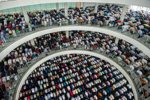 Dhaka Bangladesh 19 June 2026 Aerial view of a large crowd of men praying inside a multi level mosque with curved balconies and modern architecture.