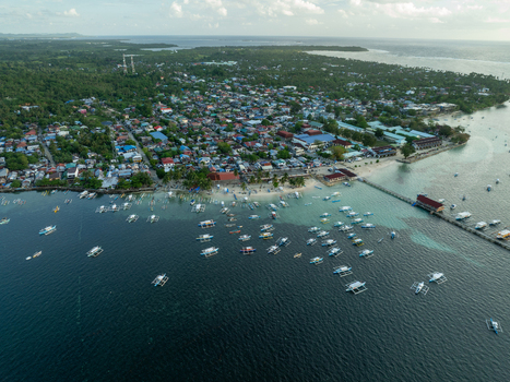 Aerial view of a coastal town with numerous traditional outrigger boats anchored in turquoise water a long pier and dense residential buildings in Siargao Philippines. Aerial view of a coastal town with numerous traditional outrigger boats anchored in turquoise water a long pier and dense residential buildings in Siargao Philippines.