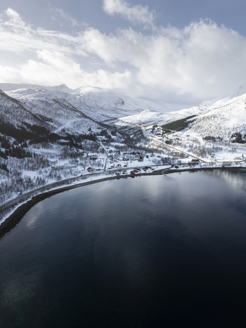 Aerial view of Grotfjord surrounded by snow covered mountains and the village of Tromvik under a cloudy sky Tromvik Troms Norway. Aerial view of Grotfjord surrounded by snow covered mountains and the village of Tromvik under a cloudy sky Tromvik Troms Norway.