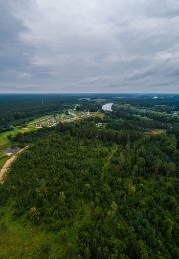 Aerial view of a lush green forest landscape with a winding river scattered rural houses and a small pond under a cloudy sky in Latvia. Aerial view of a lush green forest landscape with a winding river scattered rural houses and a small pond under a cloudy sky in Latvia.