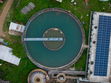 Aerial view of a circular water treatment tank with a solar panel array on the adjacent building roof surrounded by greenery in Karad Maharashtra India.