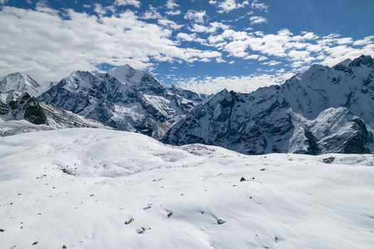 Aerial view of snow covered Himalayan mountain peaks under a bright blue sky with scattered clouds in Nepal.