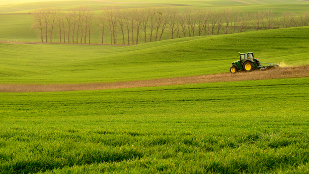 View of a green tractor working in a lush green field with rolling hills in the background in Moravia Brno City District South Moravian Region Czechia.