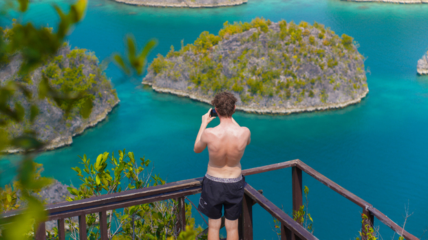 View of a man standing on a wooden viewing platform at Piaynemo taking a photo of the karst islands surrounded by turquoise water in Raja Ampat Papua Barat Indonesia. View of a man standing on a wooden viewing platform at Piaynemo taking a photo of the karst islands surrounded by turquoise water in Raja Ampat Papua Barat Indonesia.