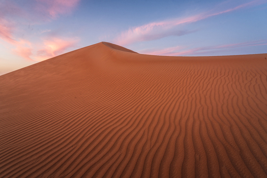 View of the Eastern Sands desert dunes with wind blown ripples under a colorful sunset sky in Oman. View of the Eastern Sands desert dunes with wind blown ripples under a colorful sunset sky in Oman.