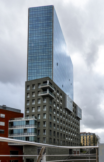 View of a modern skyscraper with a glass facade and stone base under a cloudy sky in Greater Bilbao Basque Country Spain. View of a modern skyscraper with a glass facade and stone base under a cloudy sky in Greater Bilbao Basque Country Spain.