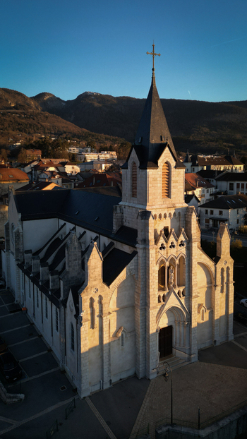Aerial view of the Eglise Saint Pierre with its tall spire and stone architecture against a backdrop of mountains during sunset in Gex Auvergne Rhone Alpes France. Aerial view of the Eglise Saint Pierre with its tall spire and stone architecture against a backdrop of mountains during sunset in Gex Auvergne Rhone Alpes France.
