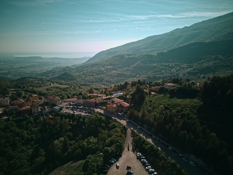 Aerial view of Lake Garda in the distance with a hillside village parking lot and lush green mountains under a clear sky Italy.