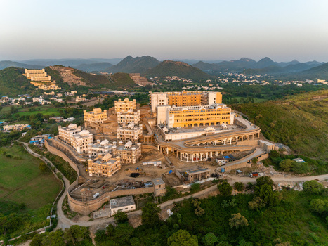 Aerial view of a sprawling resort complex with traditional architecture and terraced levels nestled in the green hills of Udaipur Rajasthan India.