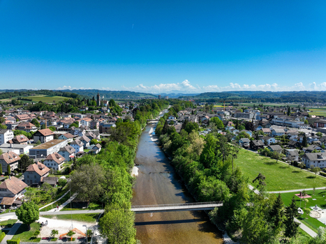 Aerial view of Emmensteg bridge crossing the Emme river surrounded by lush green trees and the town s residential buildings under a clear blue sky Kirchberg Bern Switzerland. Aerial view of Emmensteg bridge crossing the Emme river surrounded by lush green trees and the town s residential buildings under a clear blue sky Kirchberg Bern Switzerland.
