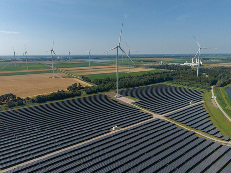 Aerial view of a large solar farm with rows of photovoltaic panels and wind turbines in the rural landscape of the Netherlands.