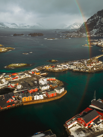 Aerial view of a vibrant rainbow arcs over the quaint fishing village and the turquoise waters of Henningsv&aelig;r Nordland Norway.