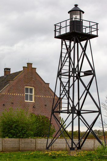 View of the historic black metal lighthouse tower and a traditional brick building under a cloudy sky in Schokland Flevoland Netherlands.