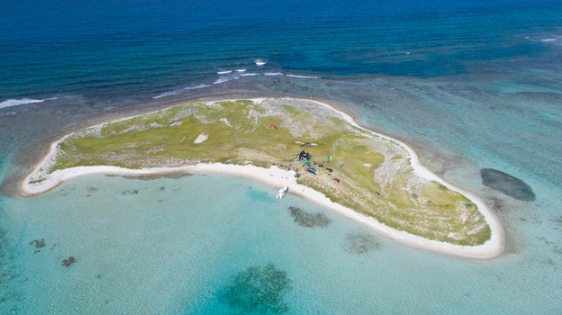 Aerial view of Los Roques archipelago featuring a small island with white sand beaches turquoise waters and kite surfers on the shore in Los Roques Dependencias Federale Venezuela. Aerial view of Los Roques archipelago featuring a small island with white sand beaches turquoise waters and kite surfers on the shore in Los Roques Dependencias Federale Venezuela.
