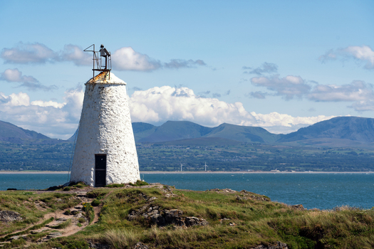 View of Twr Mawr Lighthouse on a grassy cliff overlooking the sea with mountains in the distance Isle of Anglesey Wales United Kingdom. View of Twr Mawr Lighthouse on a grassy cliff overlooking the sea with mountains in the distance Isle of Anglesey Wales United Kingdom.