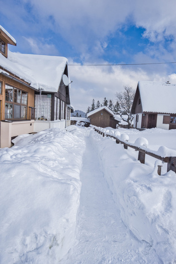 View of a snow laden path cutting through a pristine white landscape leading to quaint snow covered buildings under a bright partly cloudy sky Donovaly Slovakia. View of a snow laden path cutting through a pristine white landscape leading to quaint snow covered buildings under a bright partly cloudy sky Donovaly Slovakia.