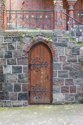 View of a historic wooden door with ornate metal hinges set into a stone wall beneath red brick architecture in Gdansk Pomeranian Voivodeship Poland. View of a historic wooden door with ornate metal hinges set into a stone wall beneath red brick architecture in Gdansk Pomeranian Voivodeship Poland.