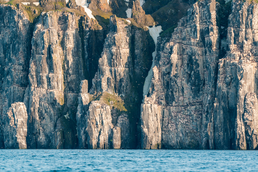 Svalbard Svalbard and Jan Mayen 22 July 2025 View of the towering basalt cliffs of Alkefjellet with thousands of nesting seabirds and patches of snow above the blue Arctic water.