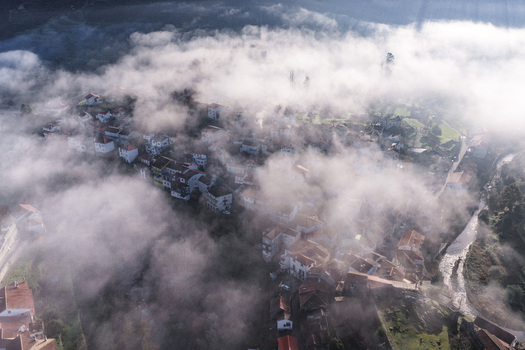 Aerial view of the historic village of Avo shrouded in thick morning mist with red tiled rooftops and a winding river in Oliveira do Hospital Coimbra District Portugal.