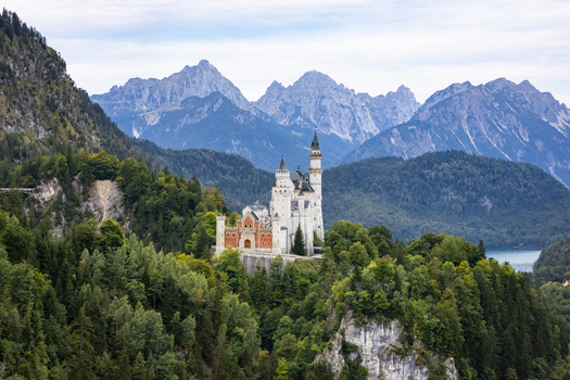 Aerial view of Neuschwanstein Castle a fairytale vision of white stone and red brick amidst emerald forests beneath jagged peaks Neuschwanstein Casle Bayern Germany. Aerial view of Neuschwanstein Castle a fairytale vision of white stone and red brick amidst emerald forests beneath jagged peaks Neuschwanstein Casle Bayern Germany.