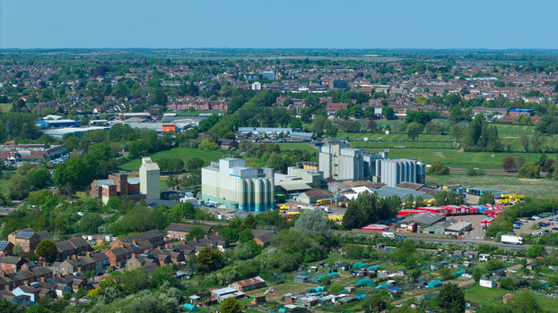 Aerial view of large industrial silos and warehouses surrounded by residential houses green trees and allotments in Little Irchester England United Kingdom. Aerial view of large industrial silos and warehouses surrounded by residential houses green trees and allotments in Little Irchester England United Kingdom.