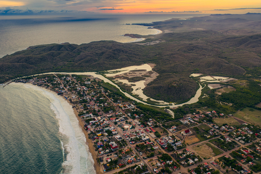 Aerial view of Punta Perula featuring the coastal town sandy beach winding estuary and surrounding hills under a golden sunset sky in Punta Perula Jalisco Mexico. Aerial view of Punta Perula featuring the coastal town sandy beach winding estuary and surrounding hills under a golden sunset sky in Punta Perula Jalisco Mexico.