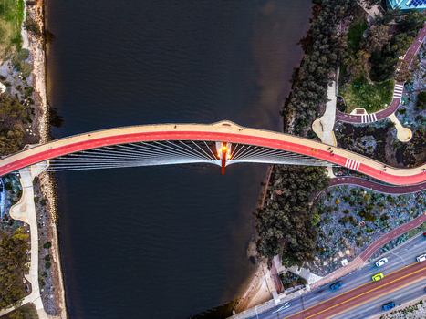 Aerial view of Boorloo Bridge spanning the Swan River with its distinctive red pedestrian path surrounded by lush parklands and nearby roads in East Perth Western Australia Australia.