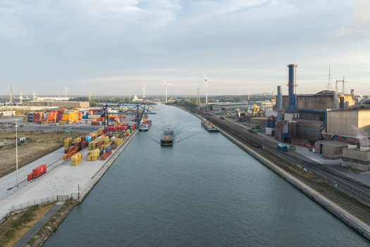 Genk Belgium 27 August 2026 Aerial view of Haven Genk container terminal with cargo ships navigating the canal industrial facilities and wind turbines under a clear sky. Genk Belgium 27 August 2026 Aerial view of Haven Genk container terminal with cargo ships navigating the canal industrial facilities and wind turbines under a clear sky.