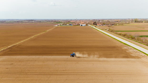 Aerial view of a lone blue tractor kicking up dust as it tills the rich brown earth contrasting against the pale sky Sremska Mitrovica Vojvodina Serbia. Aerial view of a lone blue tractor kicking up dust as it tills the rich brown earth contrasting against the pale sky Sremska Mitrovica Vojvodina Serbia.